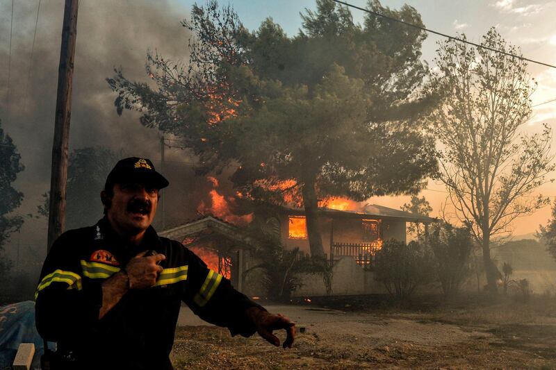 A firefighter reacts as a house burns during a wildfire in Kineta, near Athens. AFP