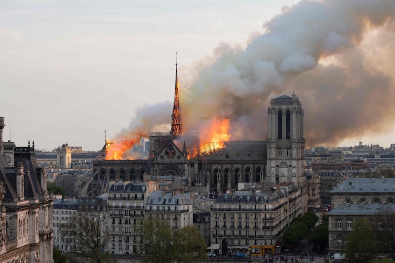 TOPSHOT - Smoke billows as flames burn through the roof of the Notre-Dame de Paris Cathedral on April 15, 2019, in the French capital Paris. A huge fire swept through the roof of the famed Notre-Dame Cathedral in central Paris on April 15, 2019, sending flames and huge clouds of grey smoke billowing into the sky. The flames and smoke plumed from the spire and roof of the gothic cathedral, visited by millions of people a year. A spokesman for the cathedral told AFP that the wooden structure supporting the roof was being gutted by the blaze. / AFP / Fabien Barrau
