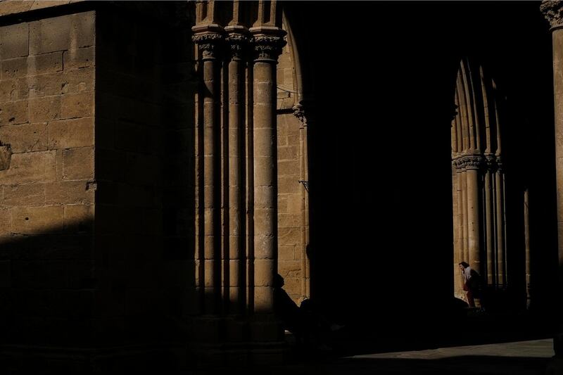 A woman, right, walks as a man, left, is silhouetted as he sits on a bench outside of the Selimiye mosque, known as the Cathedral of St Sophia until the 16th century, or Agia Sofia, in Nicosia, Cyprus, Monday, Dec. 3, 2018. (AP Photo/Petros Karadjias)