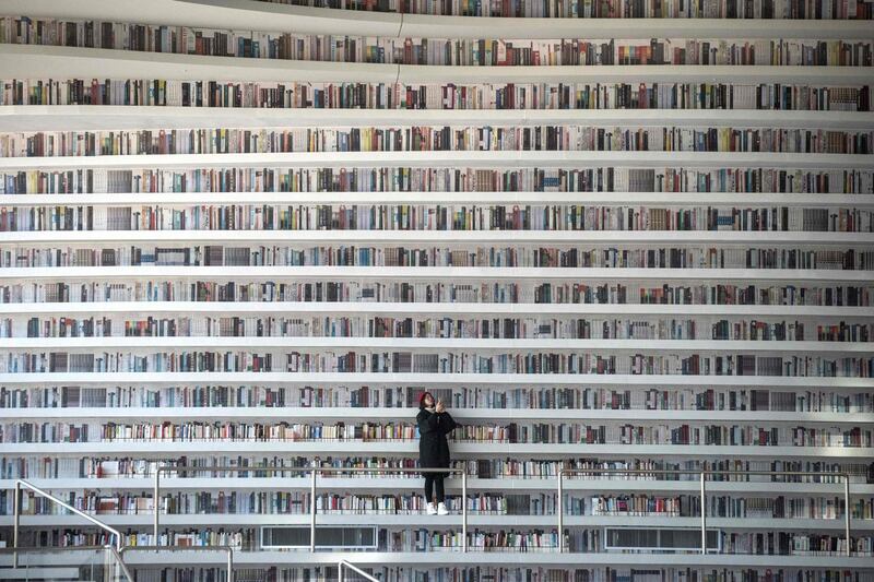 TOPSHOT - This picture taken on November 14, 2017 shows a woman taking pictures at the Tianjin Binhai Library.
A futuristic Chinese library has wowed book lovers around the world with its white, undulating shelves rising from floor to ceiling, but if you read between the lines you'll spot one problem. Those rows upon rows of book spines are mostly images printed on the aluminium plates that make up the backs of shelves. / AFP PHOTO / FRED DUFOUR / To go with AFP story China-library-architecture, FOCUS by Becky Davis