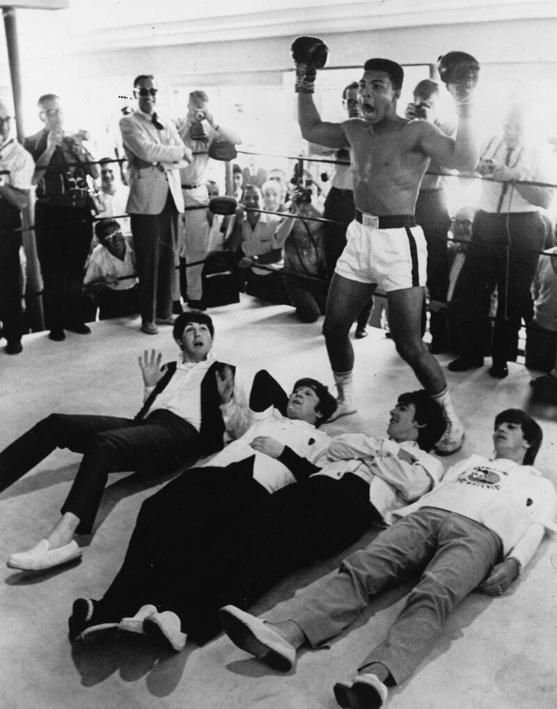 February 1964:  American heavyweight boxer Cassius Clay poses in the ring in mock victory over British pop group The Beatles, meeting the press in New York during an American tour.  (Photo by Keystone/Getty Images)