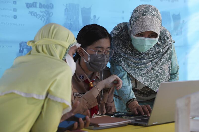 A mother, right, and her daughter, centre, use free Wi-Fi to access an online lesson inside a temporary tent in Jakarta, Indonesia. AP Photo