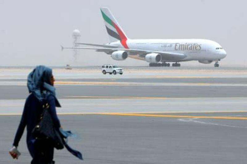A woman walks in front of an Emirates Airlines plane which landed on the runway during the media tour of Dubai's new second airport, Dubai World Central or Al-Maktoum International, operational only to cargo until passenger facilities are completed, on July 1, 2010, in the desert on the outskirts of the Gulf emirate, where a 32 million dollar (26 million euro) new "city" is being built to include a port.  AFP PHOTO/KARIM SAHIB *** Local Caption ***  919076-01-08.jpg