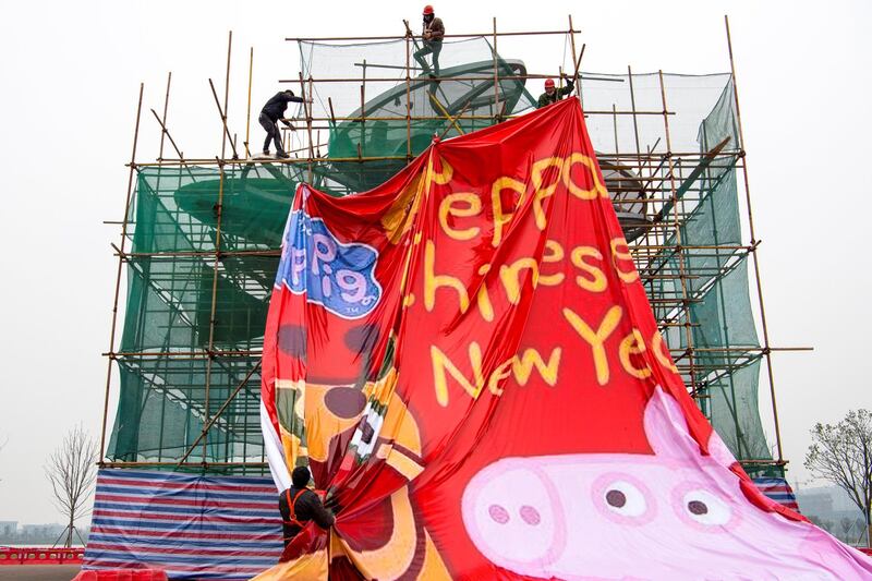 Men work on covering up a sculpture under construction with a tarpaulin with an image of Peppa Pig. Reuters