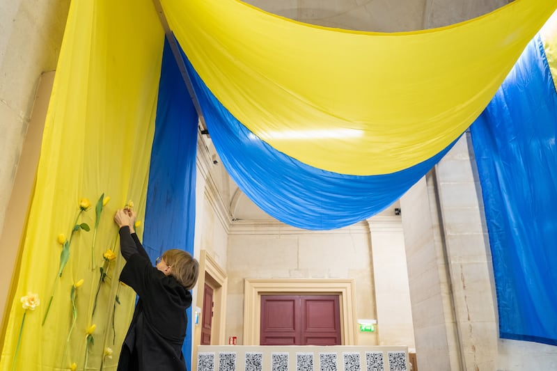 Ukrainian designer Lilia Litkovskaya sews flowers on the Ukrainian flag inside Palais de la Bourse as part of the Tranoi showcase during Paris Fashion Week, at Palais Brongniart, on March 4, 2022.