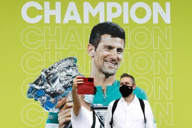 MELBOURNE, AUSTRALIA - JANUARY 17: Spectators pose for a selfie with a banner of 2021 Men's Australian Open winner Novak Djokovic of Serbia during day one of the 2022 Australian Open at Melbourne Park on January 17, 2022 in Melbourne, Australia. (Photo by Darrian Traynor / Getty Images)