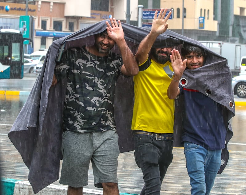 People use a canvas sheet to shield themselves from the rain on Hamdan Street, in Abu Dhabi. Victor Besa / The National