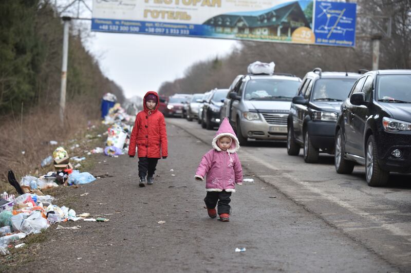 Ukrainian children walk past a line of cars heading towards the Polish border. AP