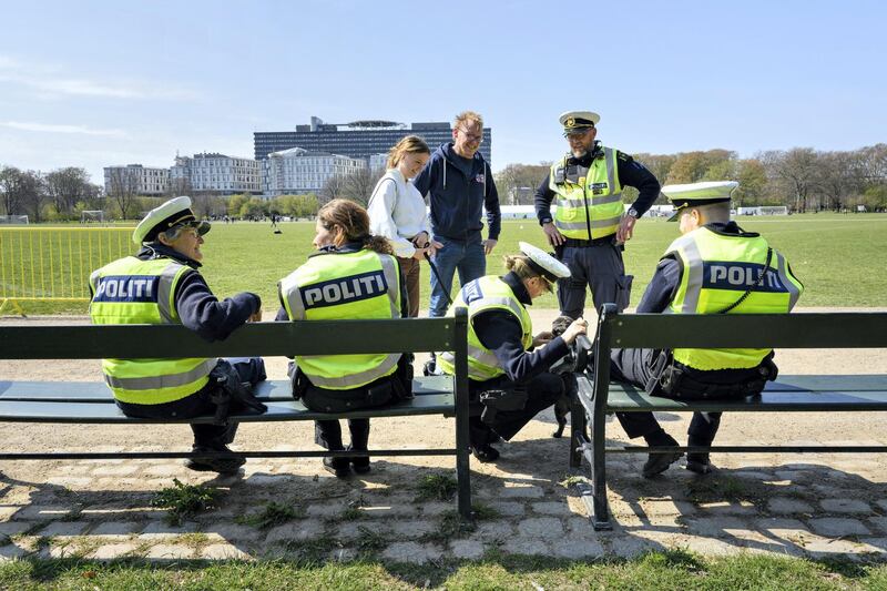 Police officers sit in the sun as they greet a dog at Faelledparken in Copenhagen, on May 1, 2021 as demonstrations and public speeches were canceled due to the ongoing coronavirus pandemic. (Photo by Philip Davali / Ritzau Scanpix / AFP) / Denmark OUT
