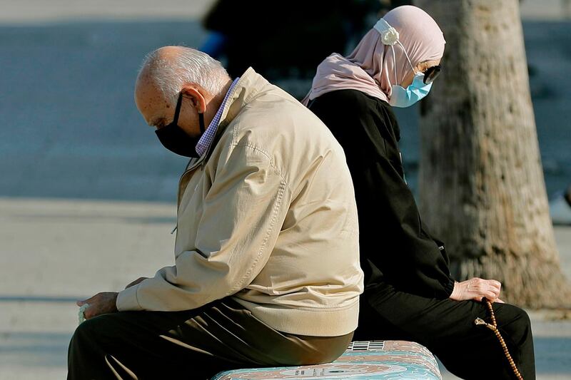 A man and a woman sit back-to-back on a bench as they enjoy a sunny day near the Beirut seaside promenade. AFP