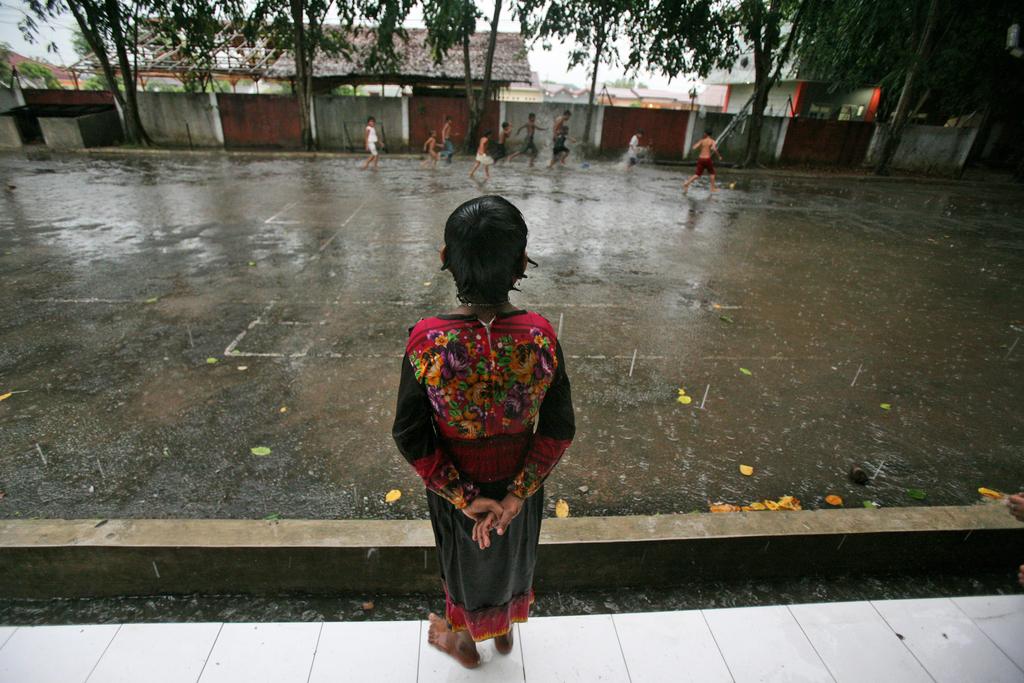 Senwara Begum watches her friends play in the rain outside their temporary shelter in Medan, North Sumatra, Indonesia. AP Photo/Binsar Bakkara