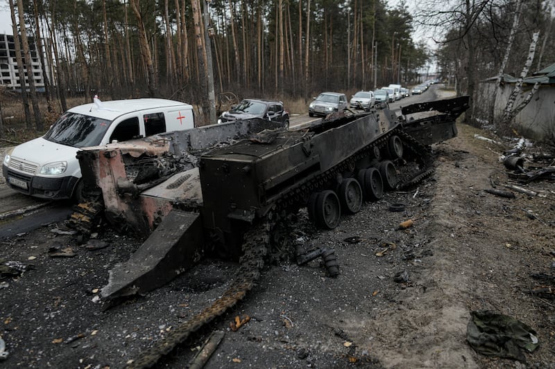 Civilian vehicles drive past a destroyed Russian tank as they leave Irpin. AP