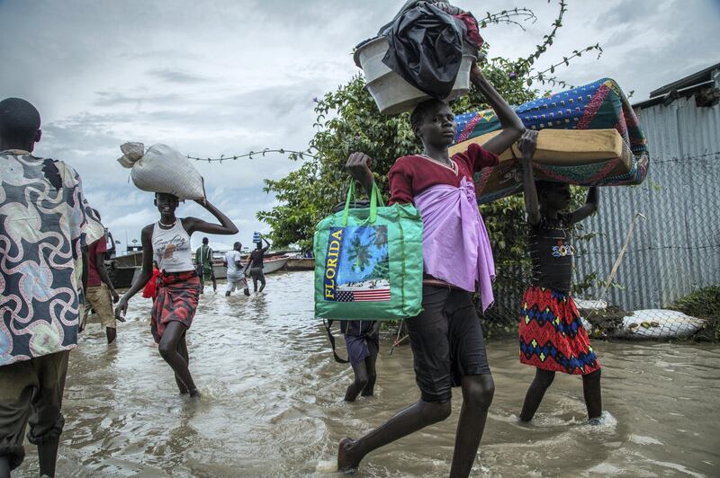 Displaced people walk with their belongings in a flooded area after the Nile river overflowed after continuous heavy rain which caused thousands of people to be displaced in Bor, central South Sudan, on August 9, 2020. (Photo by Akuot CHOL / AFP)