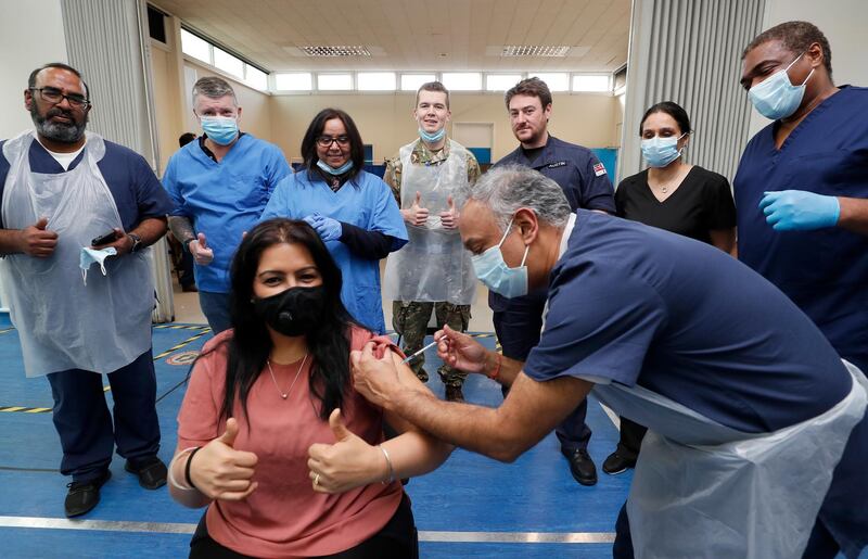 Doctor Anil Mehta, surrounded by his team of doctors, administers a dose of the Pfizer-BioNTech vaccine to Geeta Waddon to mark the 10,000th at his small practice in London. AP Photo