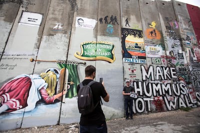 A Canadian tourist poses with a sign telling his mother he is okay as he stands against the 8 meter high separation wall built by Israel that is next to  Bansky's Walled Off Hotel in the Palestinian city of Bethlehem on November 24,2018.The barrier wall has become a giant canvas of artistic resistance .(Photo by Heidi Levine for The National).