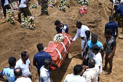 TOPSHOT - Relatives (R) watch as workers place the coffin of a bomb blast victim during a burial ceremony at a cemetery in Negombo on April 23, 2019, two days after a series of bomb attacks targeting churches and luxury hotels in Sri Lanka. Sri Lanka began a day of national mourning on April 23 with three minutes of silence to honour more than 300 people killed in suicide bomb blasts that have been blamed on a local Islamist group. / AFP / Jewel SAMAD
