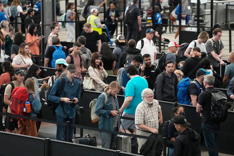 Unmasked travellers wait in long lines at a security checkpoint at Denver airport on July 5, 2022. Many airports and airlines no longer require mask use or social distancing, and many don't require pre-flight testing. David Zalubowski / AP 