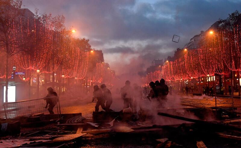 Riot police officials walk through a cloud of teargas on the Champs-Elysees in Paris during a protest by yellow vests (Gilet jaune) activists against rising oil prices and living costs. AFP