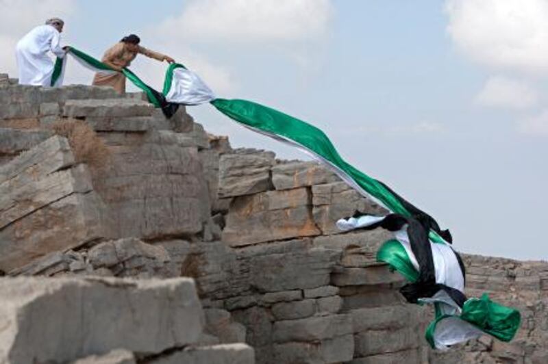 Ras al Khaimah, December 1, 2011 - Waleed Bin Shaiban al Hebsi (L) and his brother Mana (R) unfurl a 40-meter flag on Jebel Janas overlooking their father's home in Wadi Qada'a near Ras al Khaimah City, Ras al Khaimah, December 1, 2011. They made several attempts to keep the flag unfurled but the wind was not strong enough so they moved to a different location to place the flag on the mountain.(Jeff Topping/The National)
