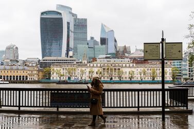 A woman walks along the Thames path in front of City of London skyscrapers in London. A rise in output in March comes a year after Britain's GDP shrank almost 20% during the nationwide lockdown last spring. EPA