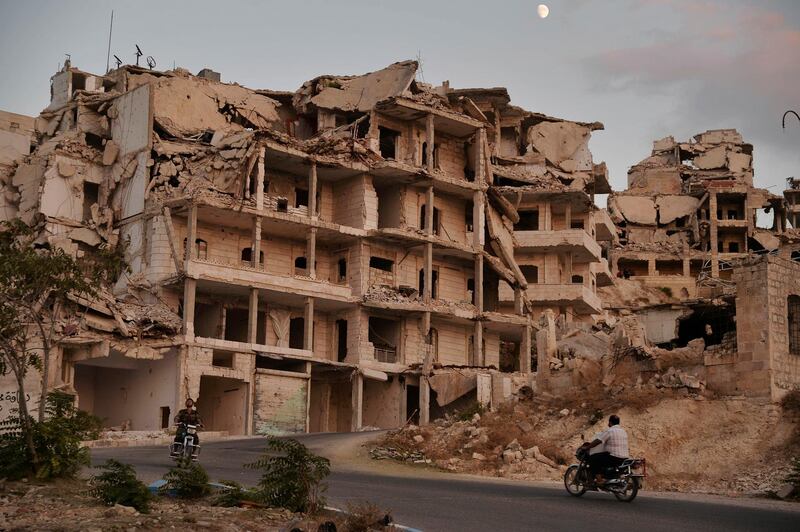 FILE - In this Thursday, Sept. 20, 2018, file, photo, motor cycles ride past buildings destroyed during the fighting in the northern town of Ariha, in Idlib province, Syria. A Syrian rebel group said Sunday, Sept. 30, 2018 that it would not pull back its fighters from front-line positions in the contested northwestern province of Idlib, where Russia and Turkey agreed to set up a demilitarized zone this month to avert an all-out offensive by Syrian government forces.(Ugur Can/DHA via AP, File)
