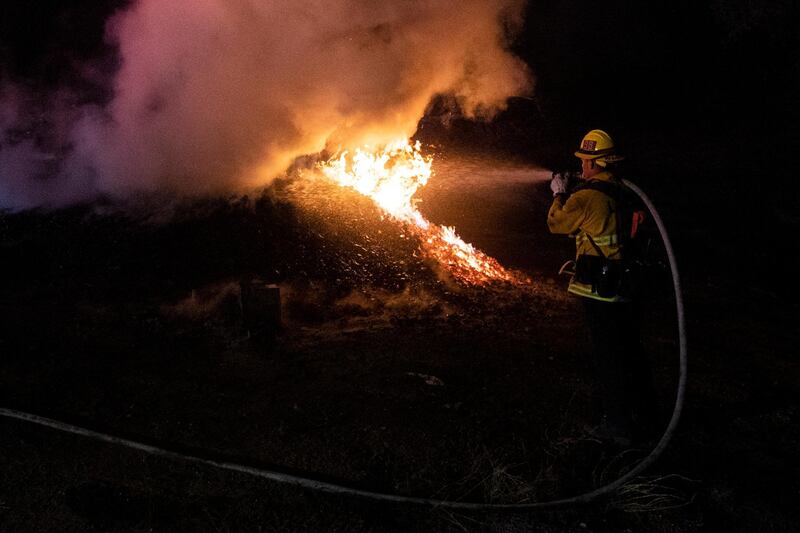 A firefighter extinguishes a brush fire lit by the Tick Fire in the hills next to a factory near Santa Clarita. EPA