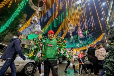 A man poses for a photo holding miniature Christmas trees along a main street in the northern suburb of Shubra (home to a large Christian population) of Egypt's capital Cairo on December 31, 2021. AFP