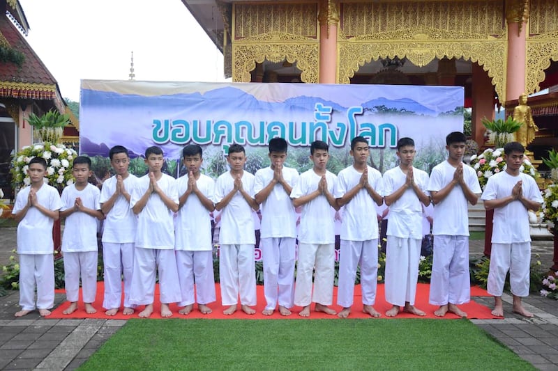 Members of Thai cave football team perform a traditional greeting in front of a backdrop with a banner reading 'Thanks to the world' during a religious worship ritual at Wat Phra Thart Doi Wao temple. Chiangrai Public Relation Office  / EPA