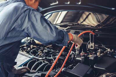 2BJ7JC0 Car mechanic holding battery electricity trough cables jumper and checking to maintenance vehicle by customer claim order in auto repair shop garage. Alamy