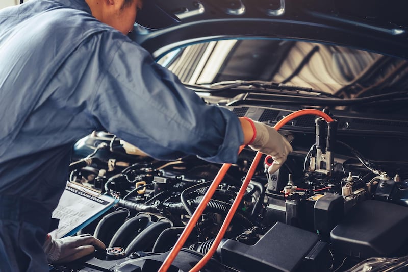 2BJ7JC0 Car mechanic holding battery electricity trough cables jumper and checking to maintenance vehicle by customer claim order in auto repair shop garage. Alamy