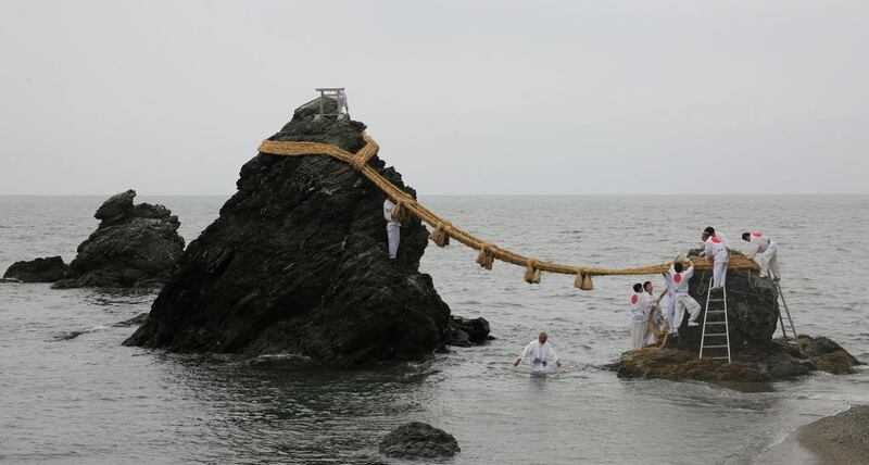 Japanese Shinto shrine priests hang the Shimenawa, Sacred ropes between God Married Stones during the Oshimenawahari ceremony of Meoto-iwa or the Couple Rock at Futami Okitama Shrine in Ise, Japan. The Oshimenawahari ceremony is held three times a year to exchange the heavy rope of rice straw that connects the Couple Rock. The Couple Rock serves as a gate to the Okitama Shrine, dedicated to the god Sarutahiko and goddess Ukanomitama from Japanese myth. Buddhika Weerasinghe / Getty Images