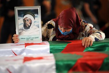 An Algerian woman holds a drawing of a fighter as she mourns over one of the national flag-draped coffins containing the remains of 24 Algerian resistance fighters decapitated during the French occupation of the country. EPA