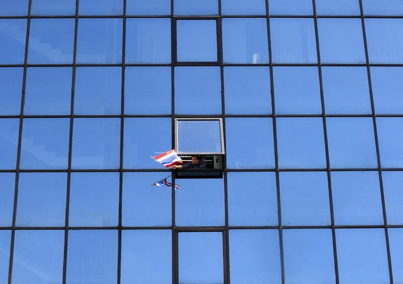 A Thai anti-government protester waves a Thai flag from an open window in a mirrored multi-storey office building as protesters led by Suthep Thaugsuban march by during a street rally in Bangkok, Thailand. Barbara Walton / EPA