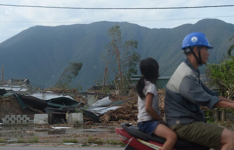 A motorcyclist and his daughter rides on a motorcycle past a raw of destroyed homes in Ky Anh town, in the central province of Ha Tinh, the day after Typhoon Doksuri makes a landfall to the country's central coast on September 16, 2017. 
Typhoon doksuri wreaked havoc on central Vietnam lashing the coast with fierce winds and heavy rains as tens of thounsands were evacuated and three people were reported dead in the country's worst storm in years. / AFP PHOTO / HOANG DINH NAM