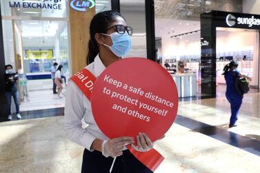 A woman wearing a protective face mask and gloves holds a sign at Mall of the Emirates. The Philippine labour office was closed for two days in Dubai after a suspected outbreak of the virus. Reuters