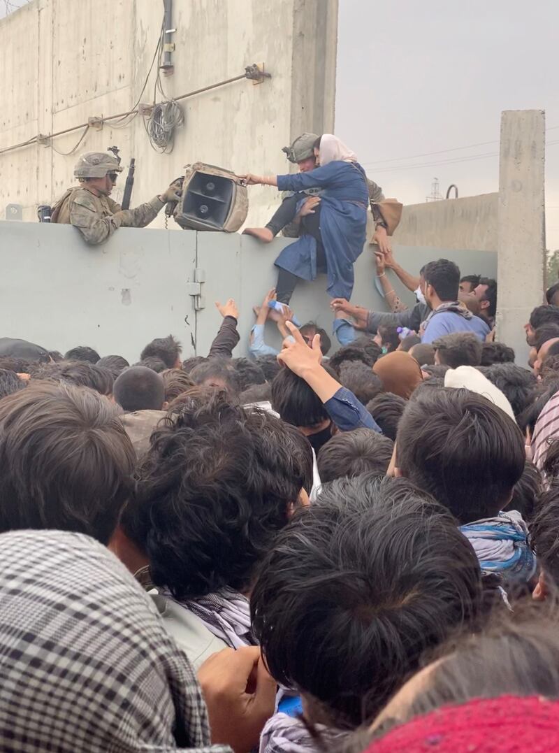 US soldiers help a woman over a wall as crowds gather at Kabul airport. Reuters
