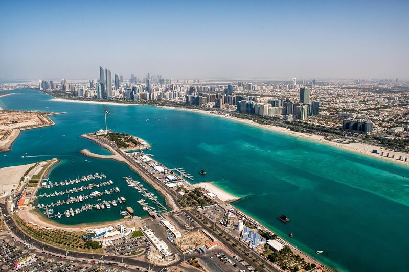 Helicopter point of view of Mosque with surrounding area in Abu Dhabi, UAE. Turquoise water, national flag and skyscrapers are also visible.