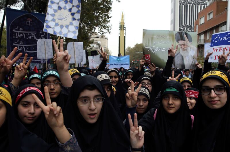 Iranian schoolgirls flash the victory sign in an annual gathering in front of the former U.S. Embassy marking the anniversary of its 1979 takeover, while a surface-to-surface Sejjil missile is displayed by the Revolutionary Guard, at rear, in Tehran, Iran, Saturday, Nov. 4, 2017. Iran on Saturday displayed a surface-to-surface missile as part of events marking the anniversary of the 1979 U.S. Embassy takeover and hostage crisis amid uncertainty about its nuclear deal with world powers. (AP Photo/Vahid Salemi)