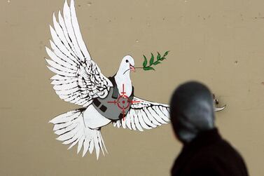 Illusive British graffiti artist named Banksy has painted new works in the West Bank town of Bethlehem, including this Peace dove in a flak jacket as a sniper takes aim at its heart, as a Palestinian woman passes and looks at the work on a Bethlehem street corner on 04 December 2007 (reissued 06 May 2020). EPA