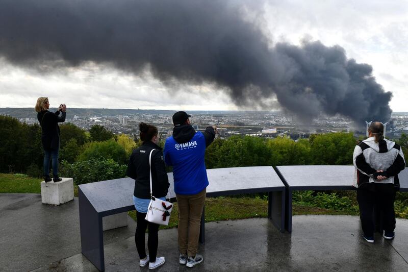 People watch black smoke rising after a fire broke at a chemical plant in Rouen, Normandy, Thursday, Sept.26, 2019. An immense mass of black smoke is rising over Normandy as firefighters battle a blaze at a chemical plant, and authorities closed schools in 11 surrounding towns and asked residents to stay indoors. (AP Photo/Stephanie Peron)