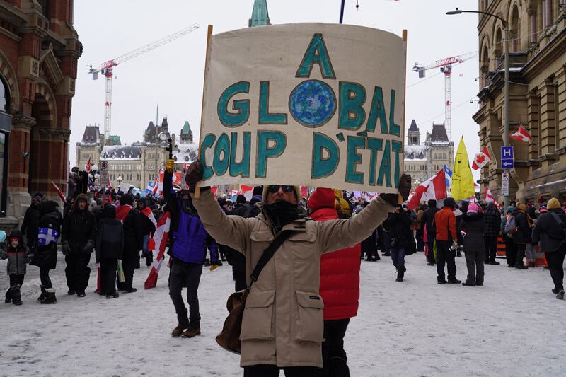 A man holds a sign reading "A global coup d'etat" at a protest in downtown Ottawa. Willy Lowry / The National.