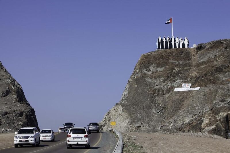 A large cut-out of the Spirit of the Union logo, which shows the seven founding Rulers, stands beside a UAE flag on top of a mountain between Khor Fakkan and Dibba. Jaime Puebla / The National