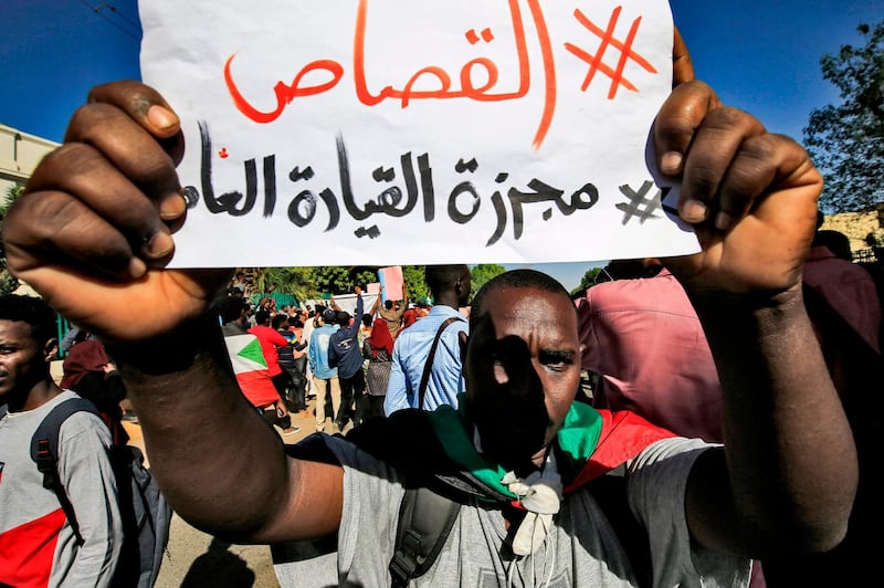 A Sudanese protester flashes a sign reading in Arabic "#Retribution, #GeneralCommandMassacre", during a demonstration in the centre of Sudan's capital Khartoum towards the prime minister's offices on November 30, 2019, calling upon authorities to deliver justice to those killed in demonstrations against the now ousted autocrat Omar al-Bashir.  / AFP / ASHRAF SHAZLY
