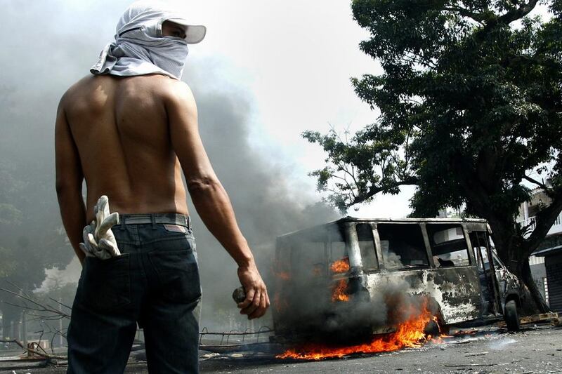 An anti-government protester holds a stone in front of a burning bus during a protest against Nicolas Maduro’s government in San Cristobal. Carlos Eduardo Ramirez / Reuters