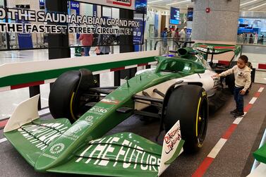 A boy hugs a race car promoting the Formula One, at the King Abdulaziz International Airport in Jiddah, Saudi Arabia, Monday, Nov.  29, 2021.  Next month's F1 race will be the first time Saudi Arabia hosts the premier sporting event, though the kingdom has hosted the lesser known Formula-E race in past years in an effort to raise the country's profile as a tourist destination.  (AP Photo / Amr Nabil)