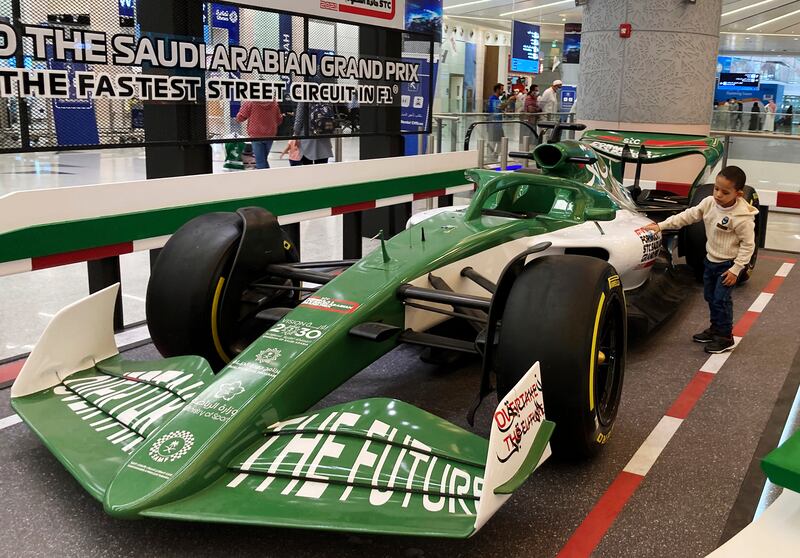 A boy hugs a race car promoting the Formula One, at the King Abdulaziz International Airport in Jiddah, Saudi Arabia, Monday, Nov.  29, 2021.  Next month's F1 race will be the first time Saudi Arabia hosts the premier sporting event, though the kingdom has hosted the lesser known Formula-E race in past years in an effort to raise the country's profile as a tourist destination.  (AP Photo / Amr Nabil)