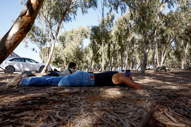 A survivor of the Nova Festival attack, May Hayat, takes cover as rocket sirens sound, during her first visit to the scene of the attack, near Re'im, Israel. Reuters