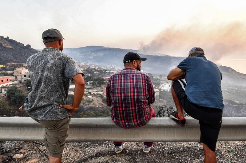 Men watch smoke rising from forest fires near the town of Melloula in north-western Tunisia, close to the border with Algeria on Monday. Wildfires raging across Algeria during a blistering heatwave have killed more than 30 people and forced mass evacuations. AFP