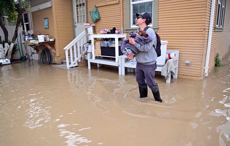 A resident carries his dog from their flooded home in the Pajaro area of Watsonville, California