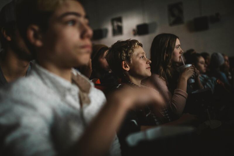 Tweens watching movie, eating popcorn and drinking soda in dark movie theater. Getty Images